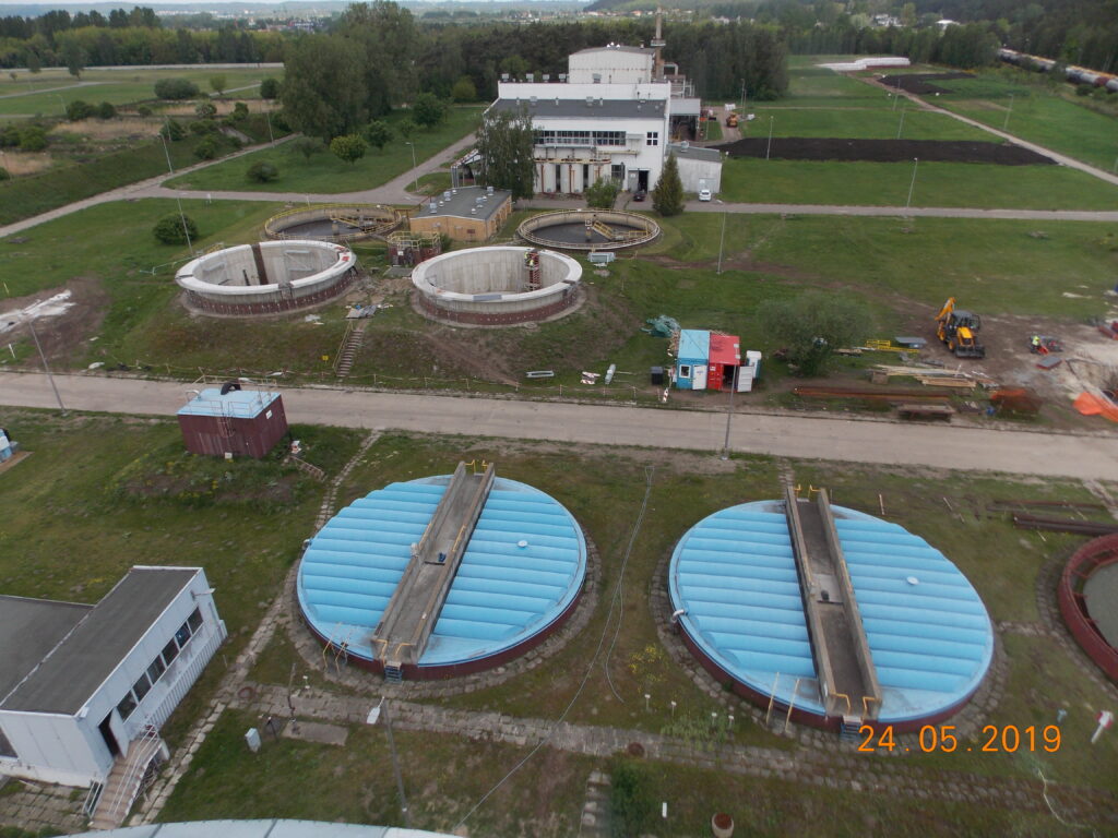 Panorama oczyszczalni ścieków z osadnikami przykrytymi niebieskimi kopułami.